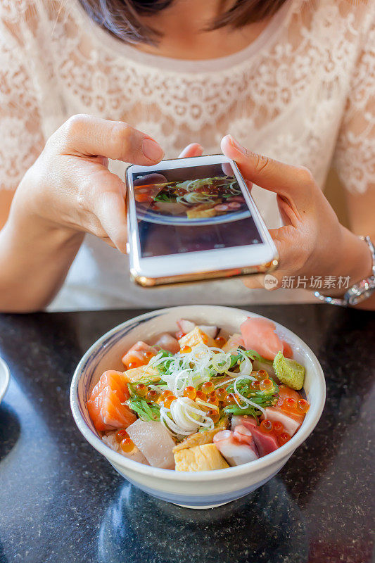 女人用智能手机摄像头拍下日式生鱼片，选择性聚焦于日式生鱼片。