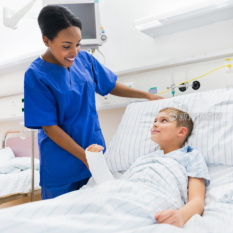一个打着石膏的孩子躺在病床上，旁边是一个穿蓝色衣服的护士