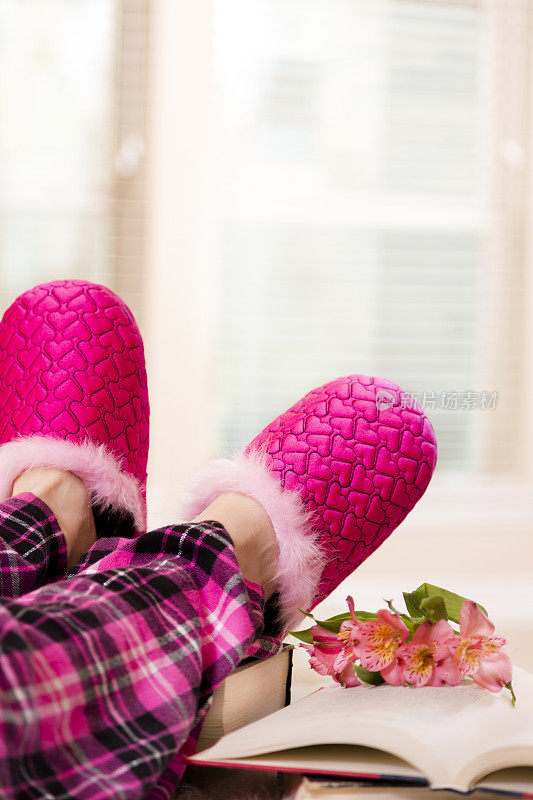 穿着睡衣和有趣的粉色拖鞋看书的女人。