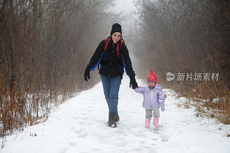 母亲和女儿徒步穿越雪林在雾天