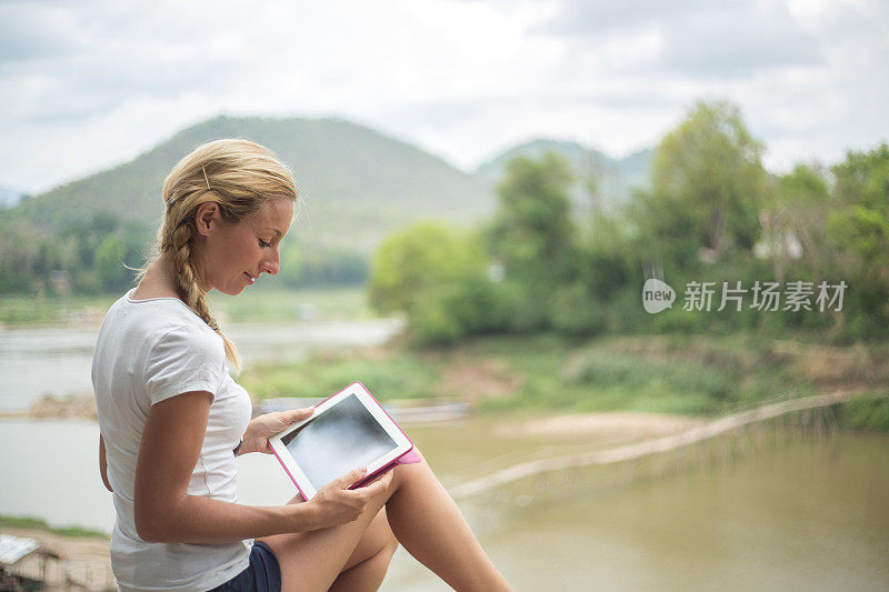 一个年轻女子在河边用她的平板电脑看书