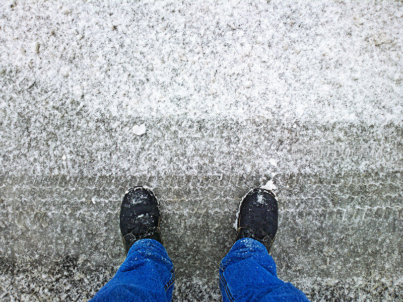 脚踩在雪地里的柏油路上。