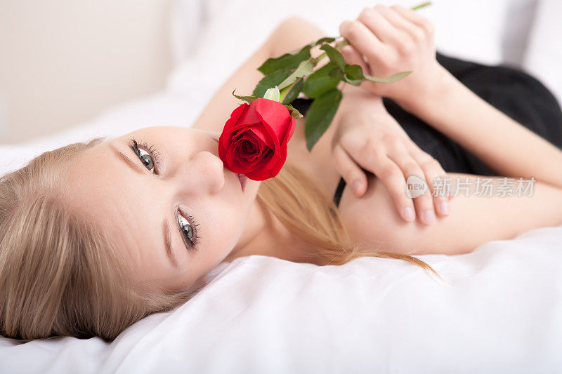 美丽的年轻女子躺在床上与红玫瑰