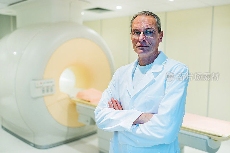一个严肃成熟的医生站在核磁共振扫描仪旁边。
