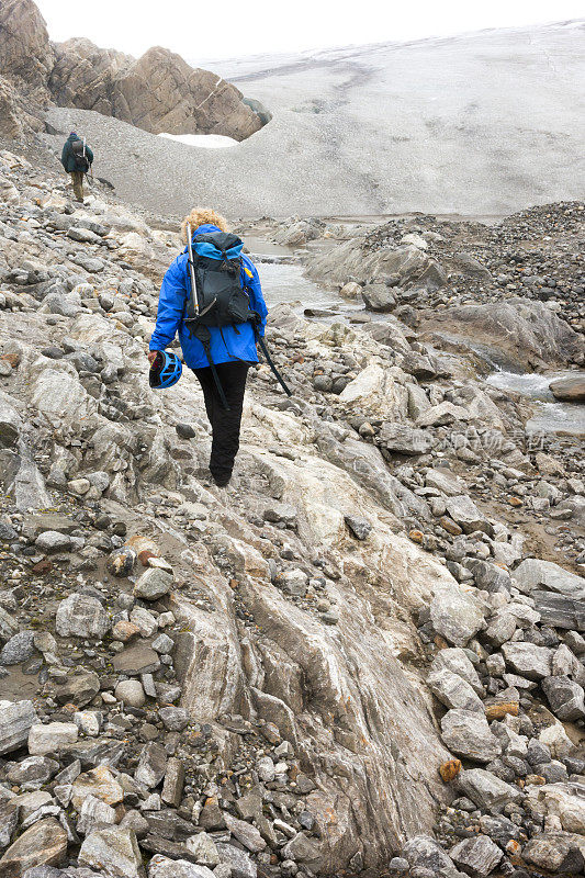 女人走过多石的冰碛走向冰川