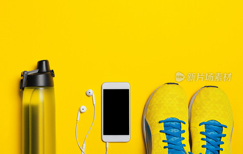 运动器材的平放镜头。黄色背景下的运动鞋、水、耳机和手机。注意力只集中在运动鞋上