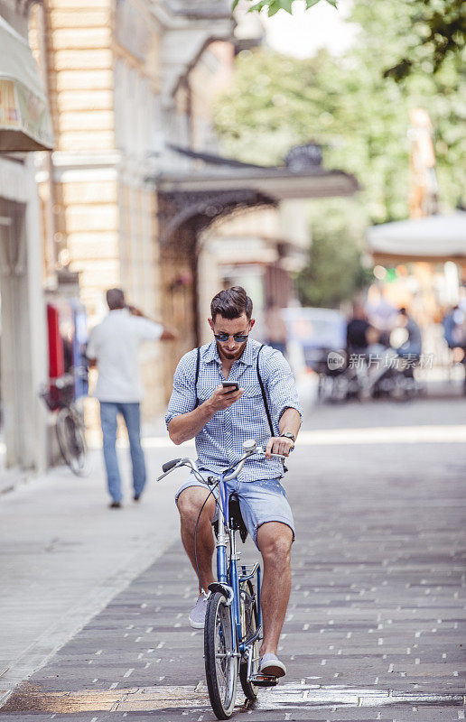 年轻时尚帅哥骑自行车和使用智能手机的肖像