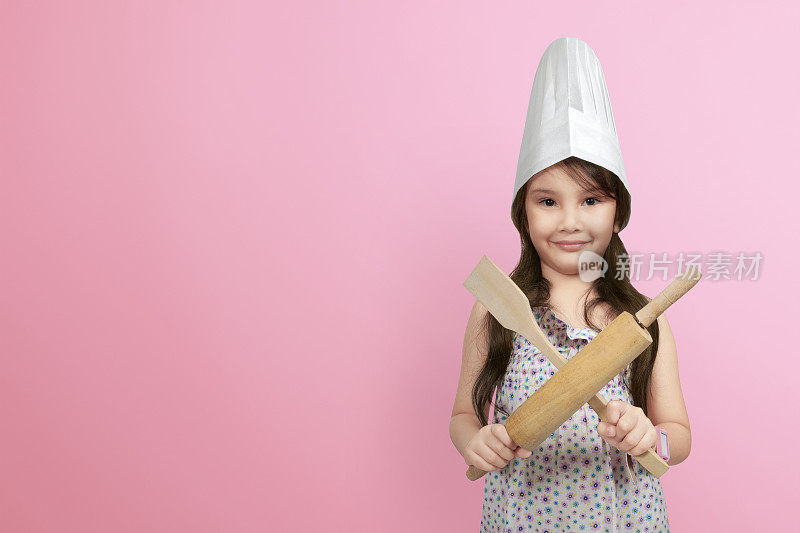 微笑的亚洲小女孩在厨师帽拿木制烹饪用具