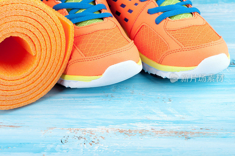 瑜伽垫和运动鞋上的蓝色木制背景。健康生活方式和运动的概念。运动设备。有选择性的重点