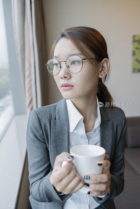 年轻女子端着一杯咖啡，望着窗外