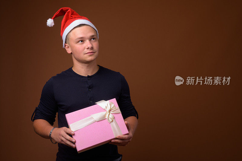 在彩色背景下，一个年轻英俊的男子拿着粉色的礼盒，戴着圣诞帽