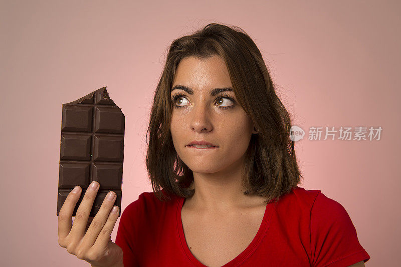 年轻美丽快乐和兴奋的女人拿着大巧克力棒思考感觉诱惑看起来内疚不节食