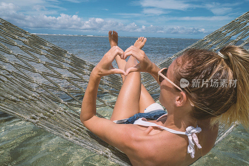 在海上的吊床上做心形手指架的女人