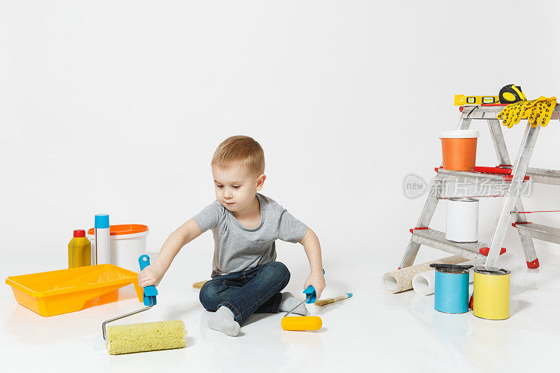 可爱的小男孩坐在地板上，用仪器装修公寓房间孤立的白色背景。墙纸，胶水配件，绘画工具。修复。为人父母,童年的概念。