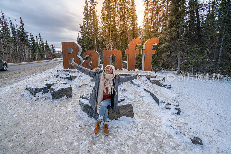 在加拿大班夫镇，一名年轻女子在欢迎来到班夫的标牌前摆姿势