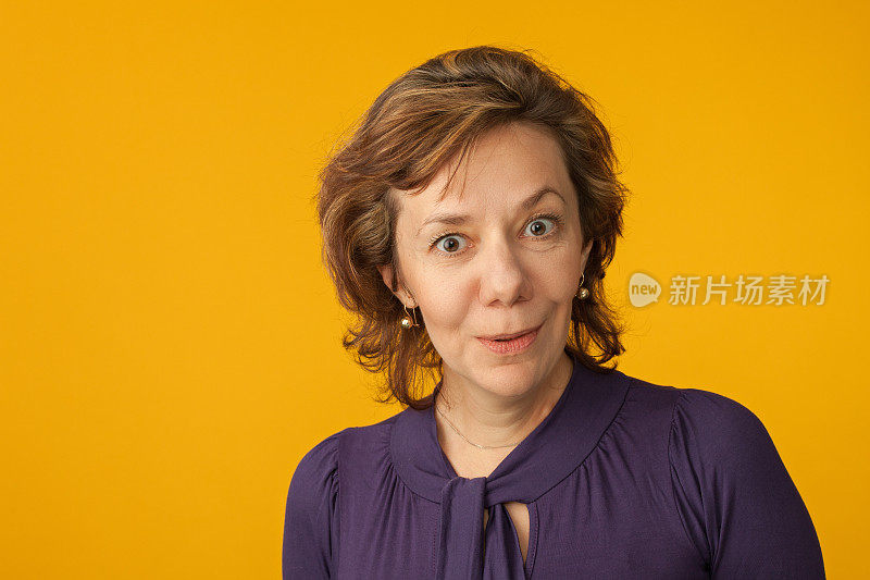 一个40岁的女人在黄色的背景上穿着紫色的衬衫的工作室肖像