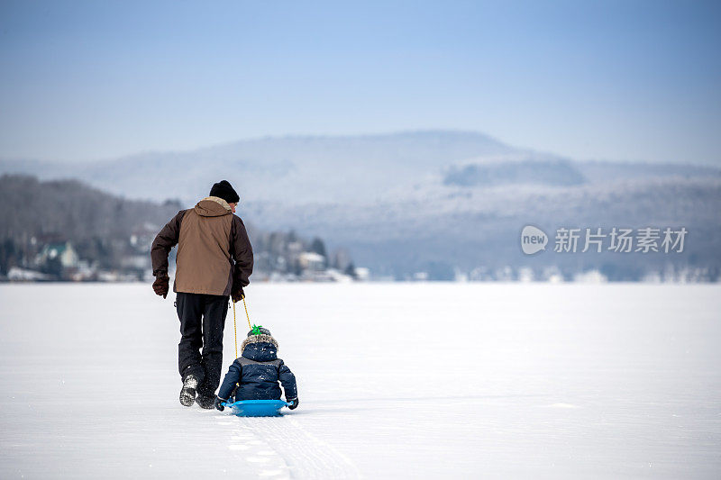 冬天，爷爷在冰湖上拉着孙子的雪橇