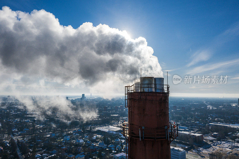 暖气站的烟囱和烟雾弥漫在冬天蓝色的天空中