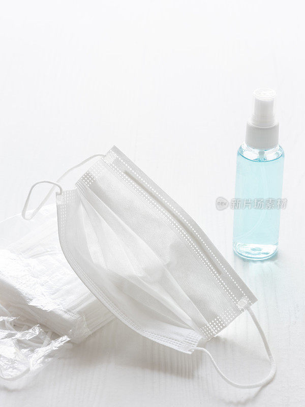 外科口罩，旁边是一包口罩和一瓶洗手液，在白色的桌子背景上，选择聚焦，聚焦在前景的口罩上。