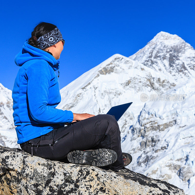 一名女子在喜马拉雅山使用笔记本电脑，背景是珠穆朗玛峰