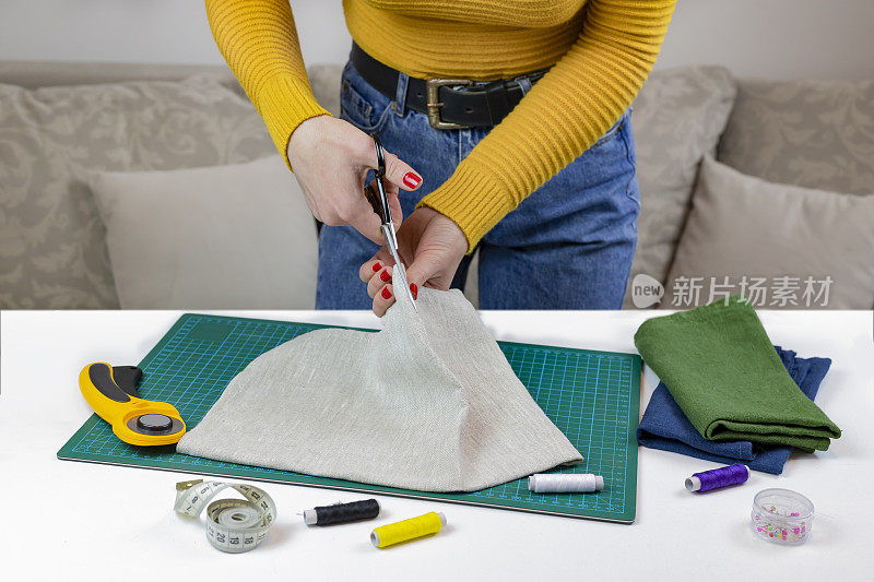穿黄色毛衣的女人剪布料。桌子上有缝被子的工具。拼布刀、剪刀、衬里剪垫、自锁、线、卷尺。缝纫用品