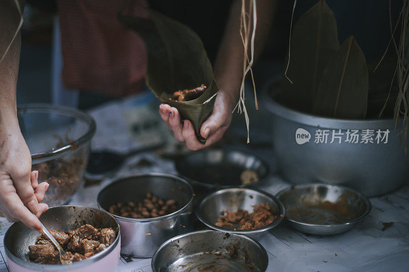 一位年长的亚洲华人妇女在她的厨房里准备粽子，把配料包好，为端午节做准备