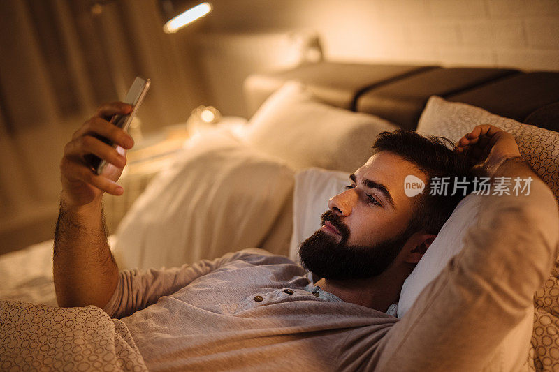 英俊的大胡子男人晚上在床上用手机