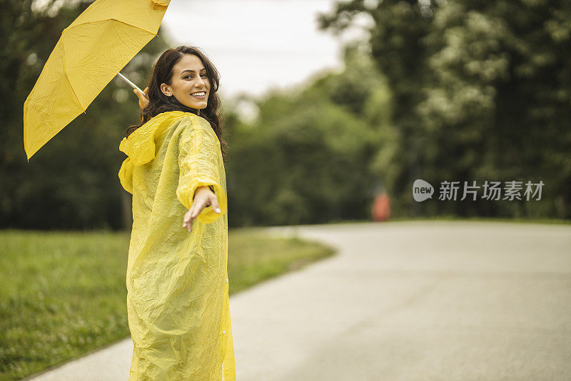 拿着黄伞，穿着黄雨衣，享受着雨的女人