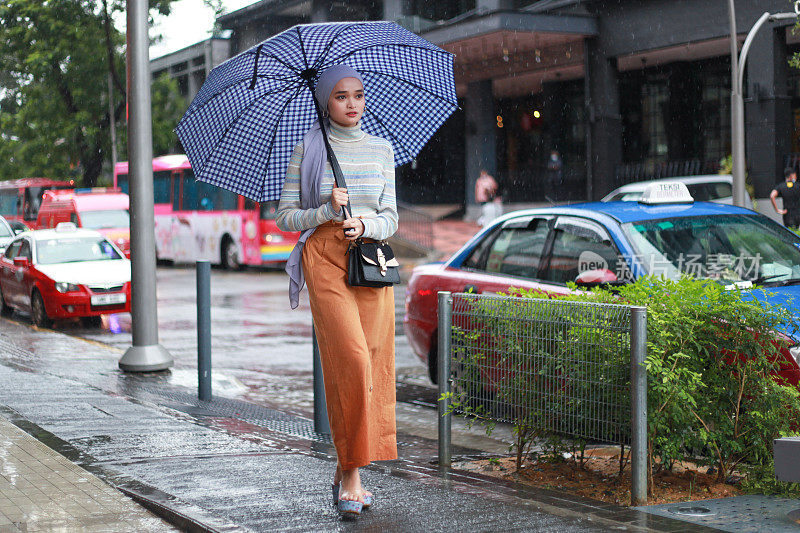 一位戴着头巾、撑着伞的穆斯林马来妇女在雨中行走