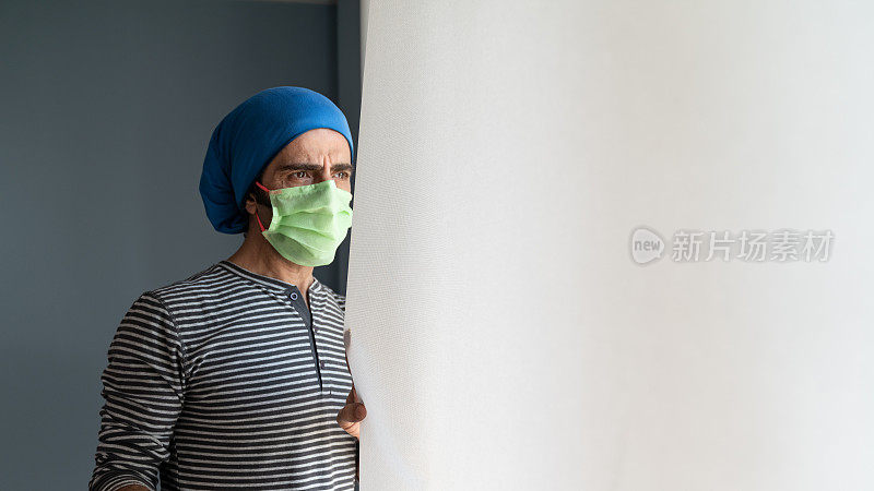 冠状病毒隔离的成年男子戴防护口罩站在窗边