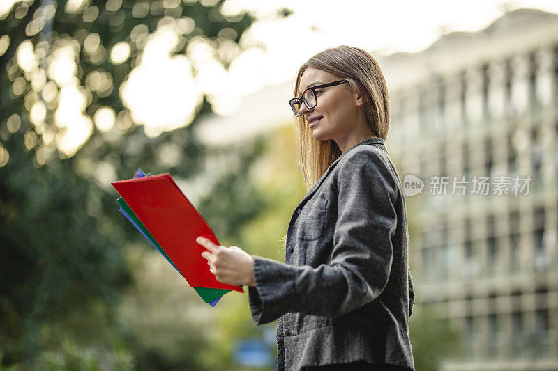 肖像自信的商业女性拿着和阅读文件在户外