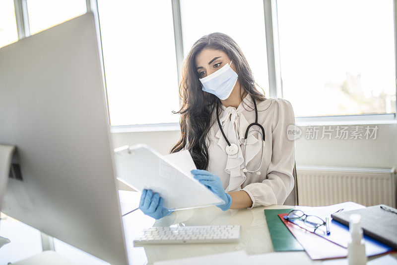 年轻女医生在她的办公室工作，使用电脑和阅读医疗文件