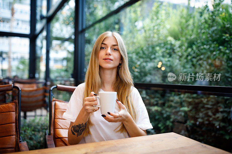 年轻的金发女子在咖啡馆喝咖啡