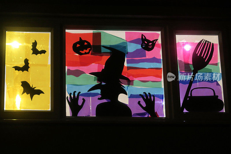 万圣节场景的窗户图片，背光女巫剪影与蝙蝠，坩埚，扫帚，南瓜和猫描绘在窗玻璃上，薄纸彩色玻璃效果艺术