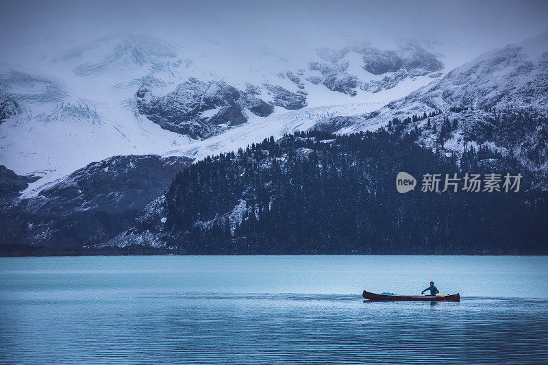 在阴沉阴沉的天气里，人们在平静的湖面上划独木舟。