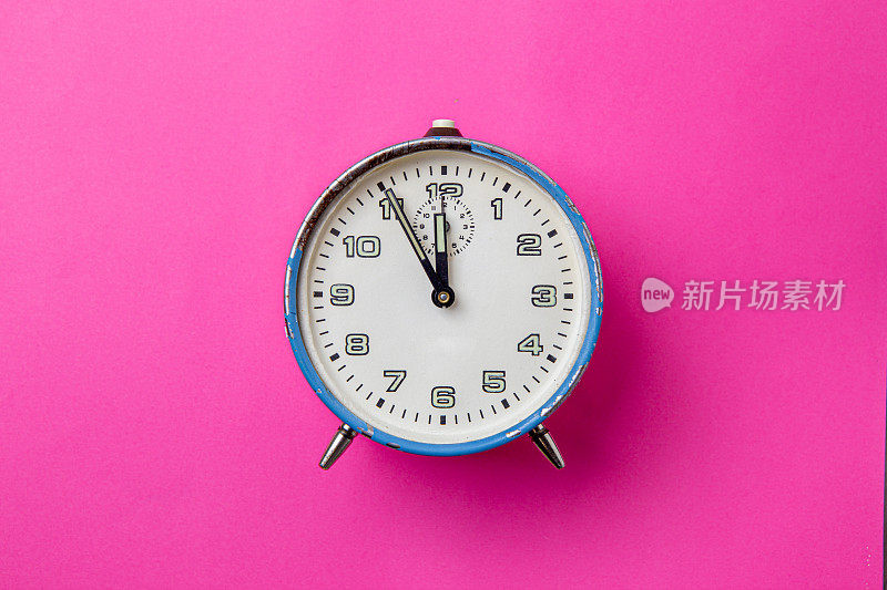 旧的复古模拟蓝色闹钟在一个粉红色的背景。钟从5分钟到12点开始。