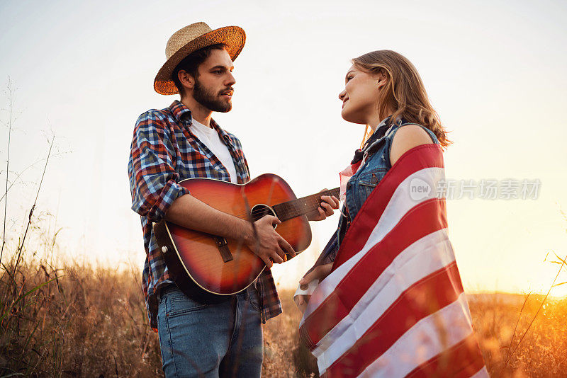 在日落时分，一个男人在球场上弹吉他，给他的女朋友唱歌