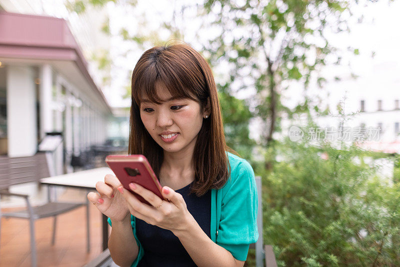 穿着绿色羊毛衫的日本女人在户外咖啡馆使用智能手机