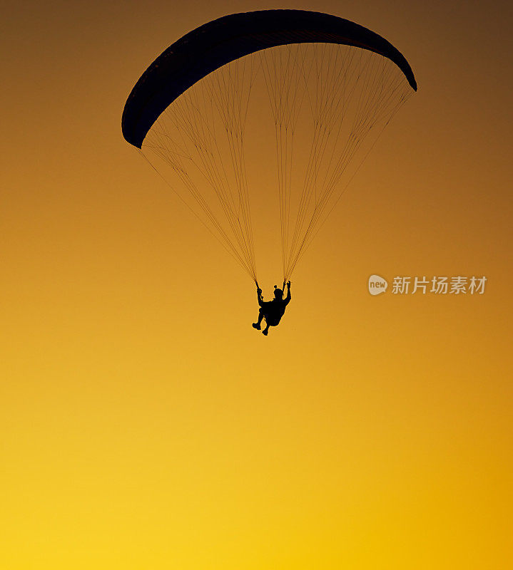 黑色剪影的滑翔伞飞行在晴朗的傍晚黄色的天空背景，背面阳光