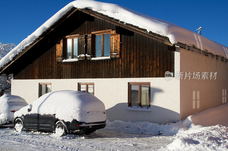 德国阿尔卑斯山典型的冬天的木屋，屋顶上有很多雪，前面有一辆被雪覆盖的汽车