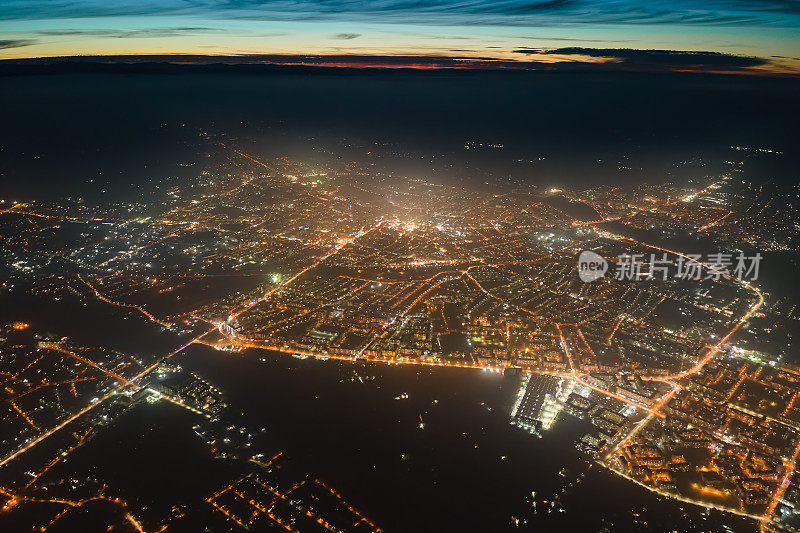 从飞机窗口鸟瞰图的建筑物和明亮的照明街道在城市居民区夜间。高海拔的黑暗城市景观