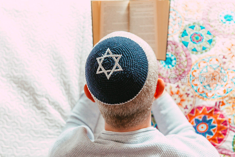 犹太男子戴着头盖骨帽在家里读圣经