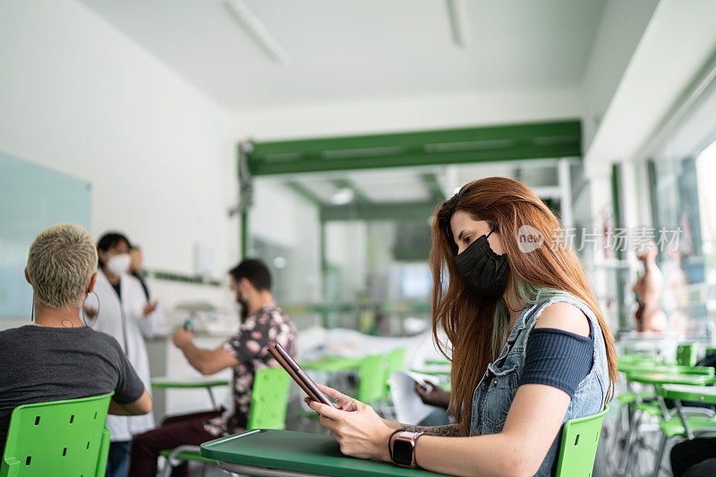 年轻的女学生使用数码平板电脑在教室里学习——使用口罩