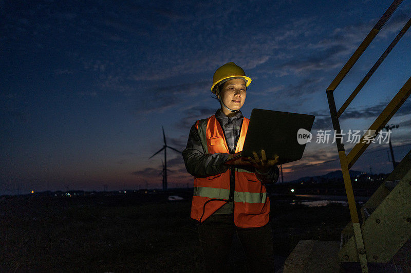一位夜班的亚洲女性风力发电技术人员用一台笔记本电脑对风力涡轮机进行故障检修
