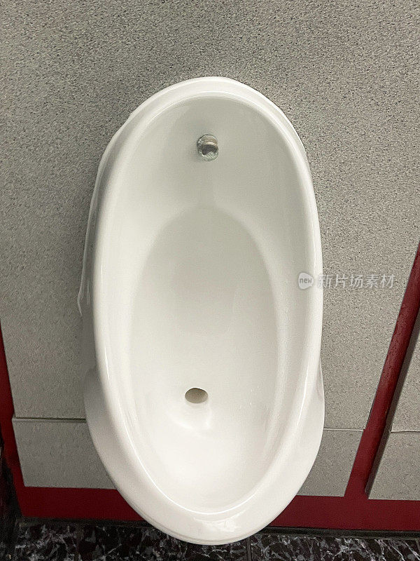 公共厕所厕所的个人小便器特写图像，白色陶瓷小便器排成一排，大理石瓷砖背景挡板，清洁卫生的小便器排水沟和排水沟内墙，石灰华瓷砖石材地板
