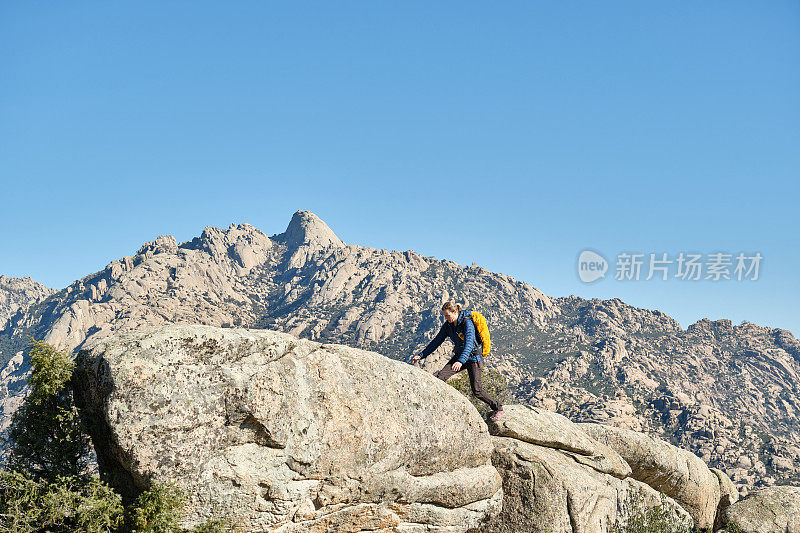 一个背着背包的女人从山上的岩石上跳下来