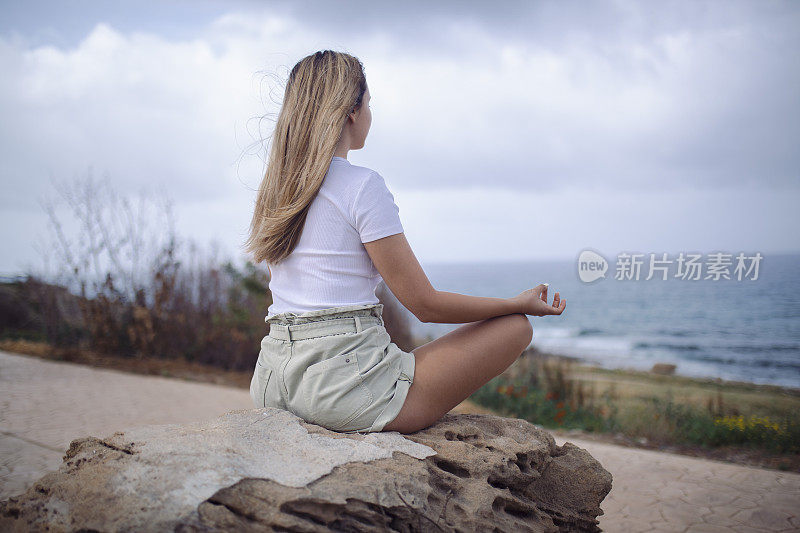 一位身穿白色t恤的陌生女子坐在一块岩石上冥想。