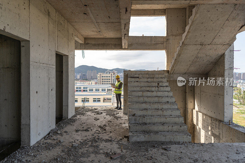 一名亚洲女性建筑工程师在一栋未完工的建筑里用笔记本电脑工作