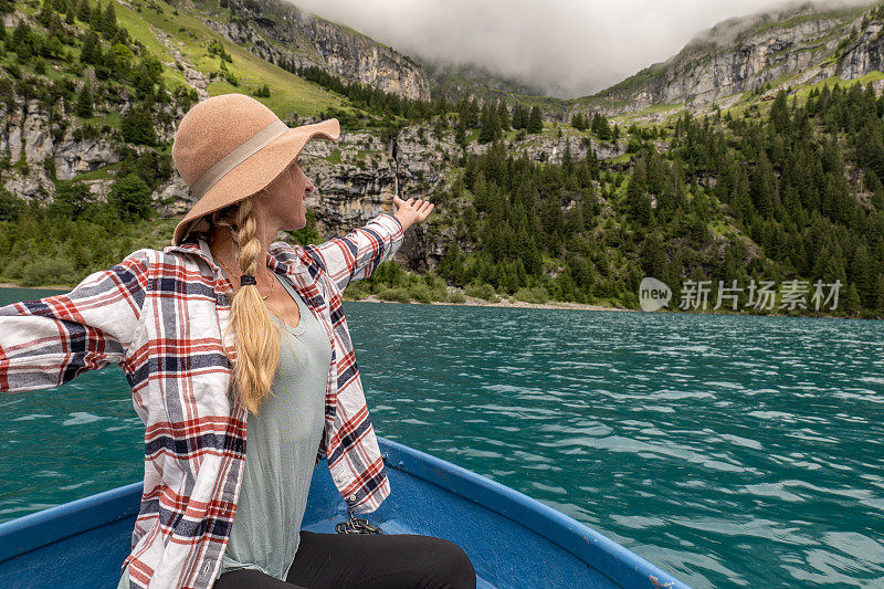 快乐的年轻女子张开双臂，在夏天的高山湖泊上划船