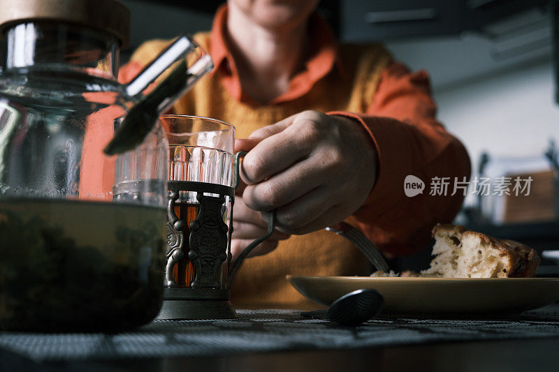 女人坐在厨房里，喝着热茶，吃着自制的梅子糕，用着智能手机